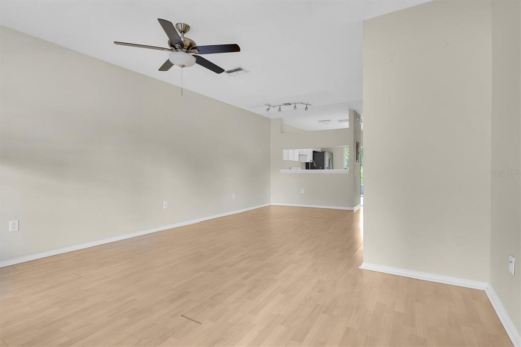 An empty living room with light wood-look flooring, a ceiling fan, and a kitchen pass-through — 1338 STANDRIDGE DRIVE, ZEPHYRHILLS, FL