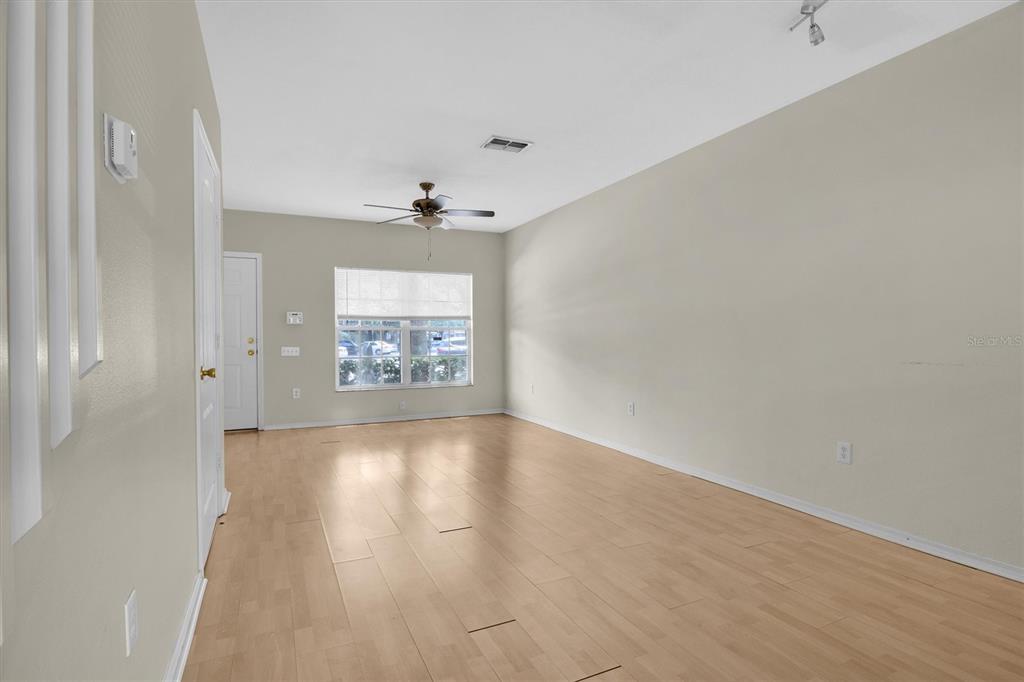 An empty living room features light wood-look flooring, beige walls, a ceiling fan, and a window — 1338 STANDRIDGE DRIVE, ZEPHYRHILLS, FL