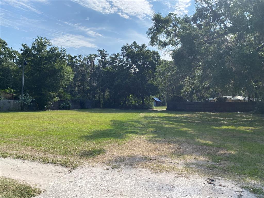 A grassy, vacant lot is enclosed by wooden fences and surrounded by mature trees — US HWY 301, OXFORD, FL