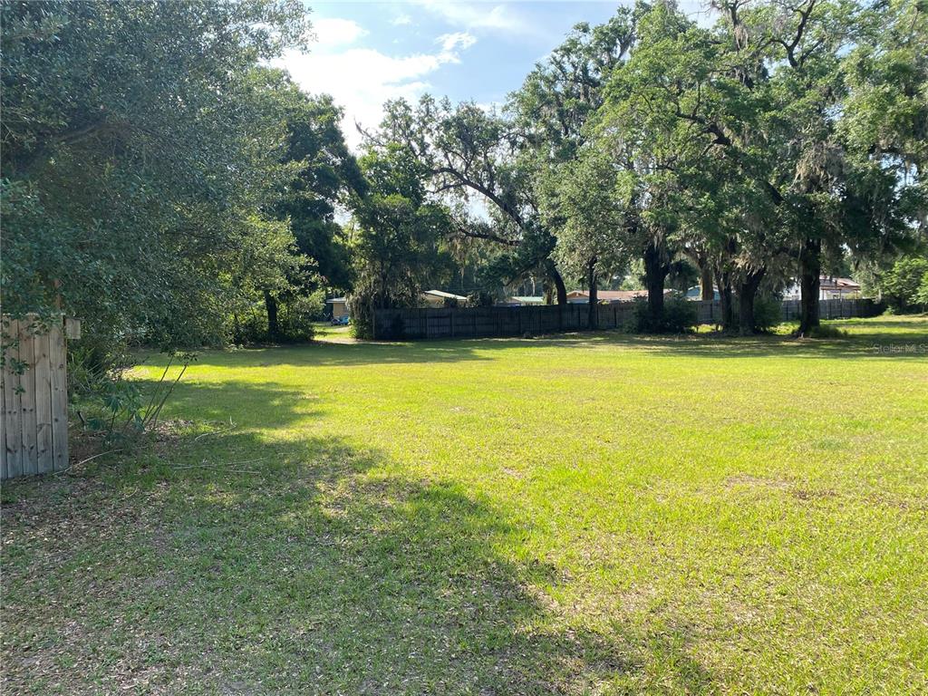 A large, grassy, vacant residential lot is bordered by trees and a wooden fence — US HWY 301, OXFORD, FL
