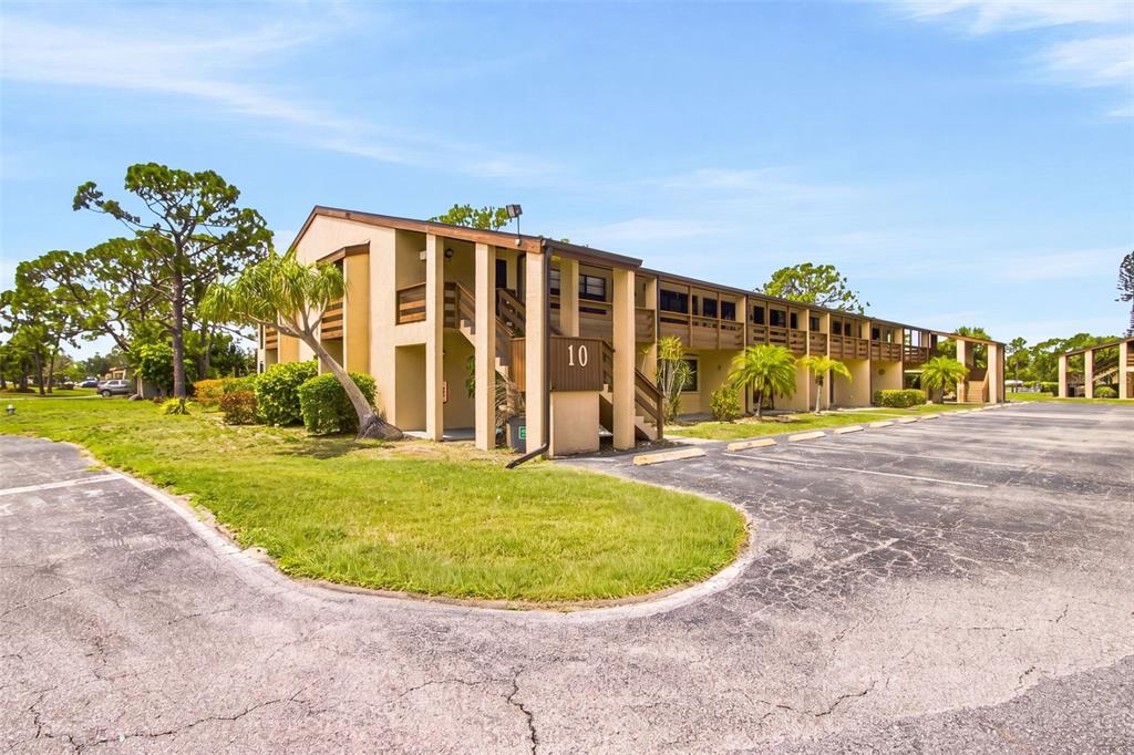 A two-story apartment building with tan stucco walls and an outdoor staircase — 10 QUAILS RUN BOULEVARD UNIT 8, ENGLEWOOD, FL