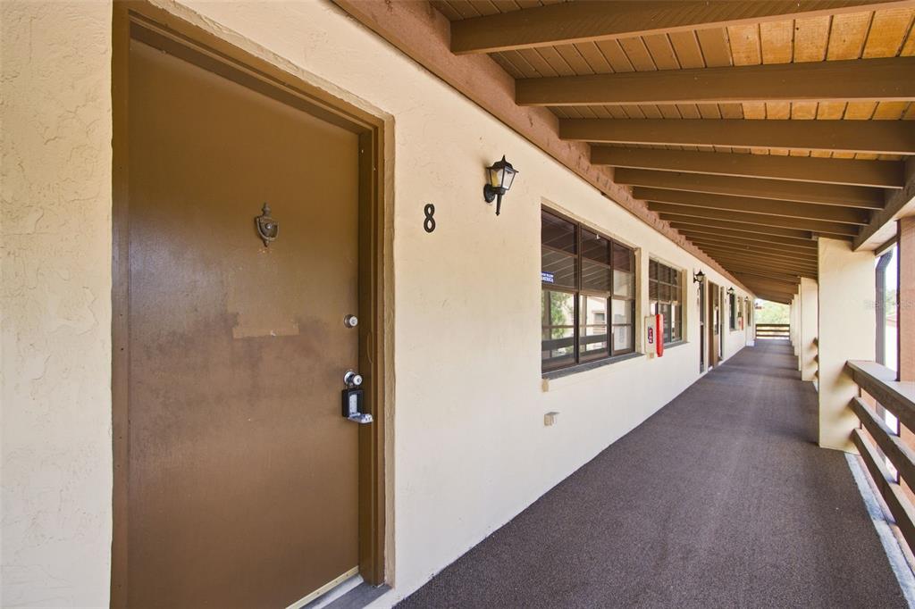 An outdoor apartment building walkway features a brown door labeled number eight and wooden beams — 10 QUAILS RUN BOULEVARD UNIT 8, ENGLEWOOD, FL