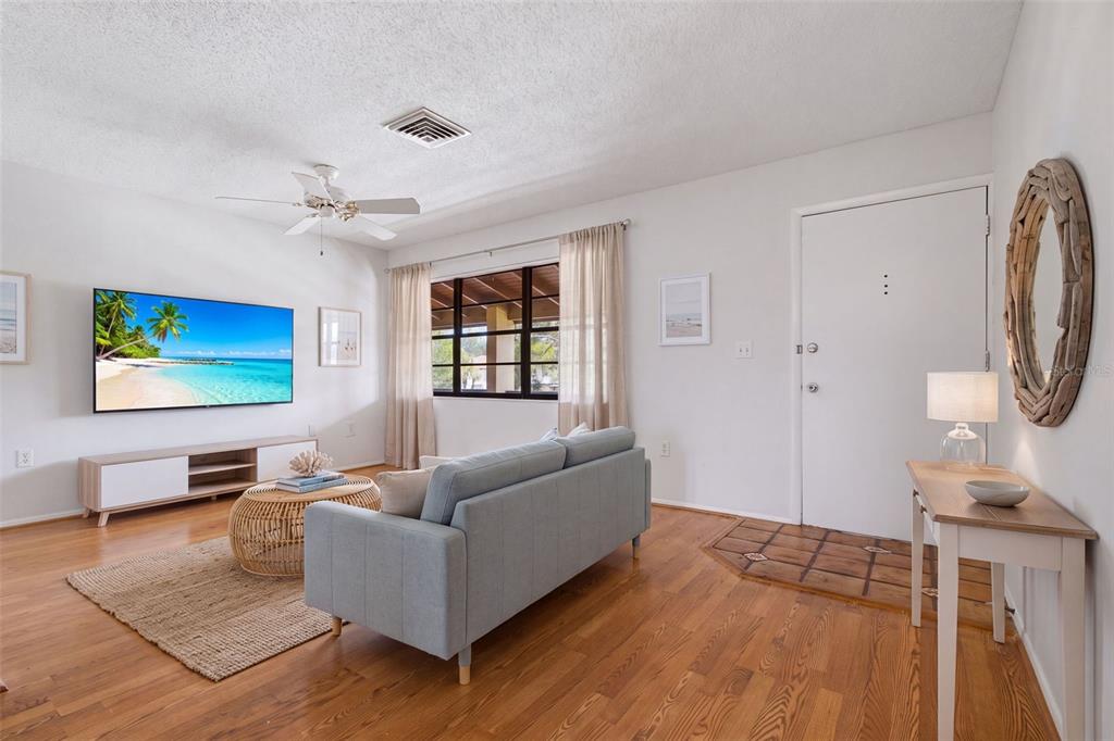 A living room features hardwood floors, a light blue sofa, a television, and a front door — 10 QUAILS RUN BOULEVARD UNIT 8, ENGLEWOOD, FL