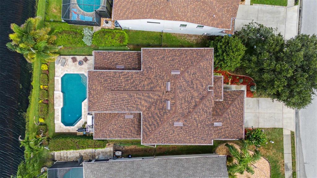 A swimming pool with a stone spa overlooks a lake at sunset with palm trees — 1231 KETZAL DRIVE, TRINITY, FL