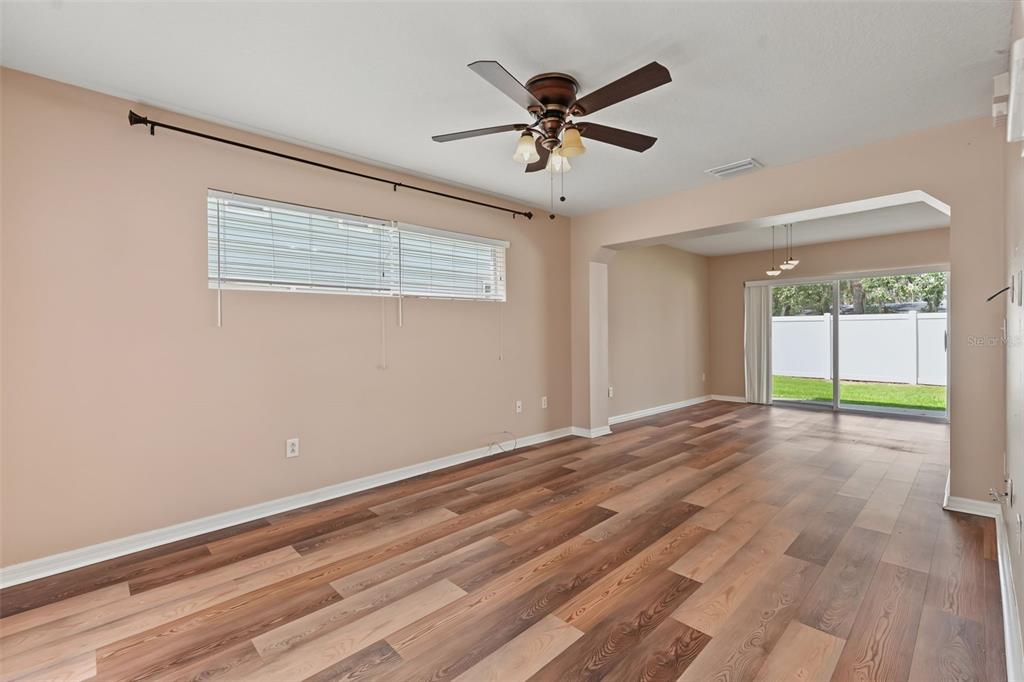 An empty living room features wood-look flooring, a ceiling fan, and sliding glass doors to outside — 150 SAWTOOTH DRIVE, VALRICO, FL