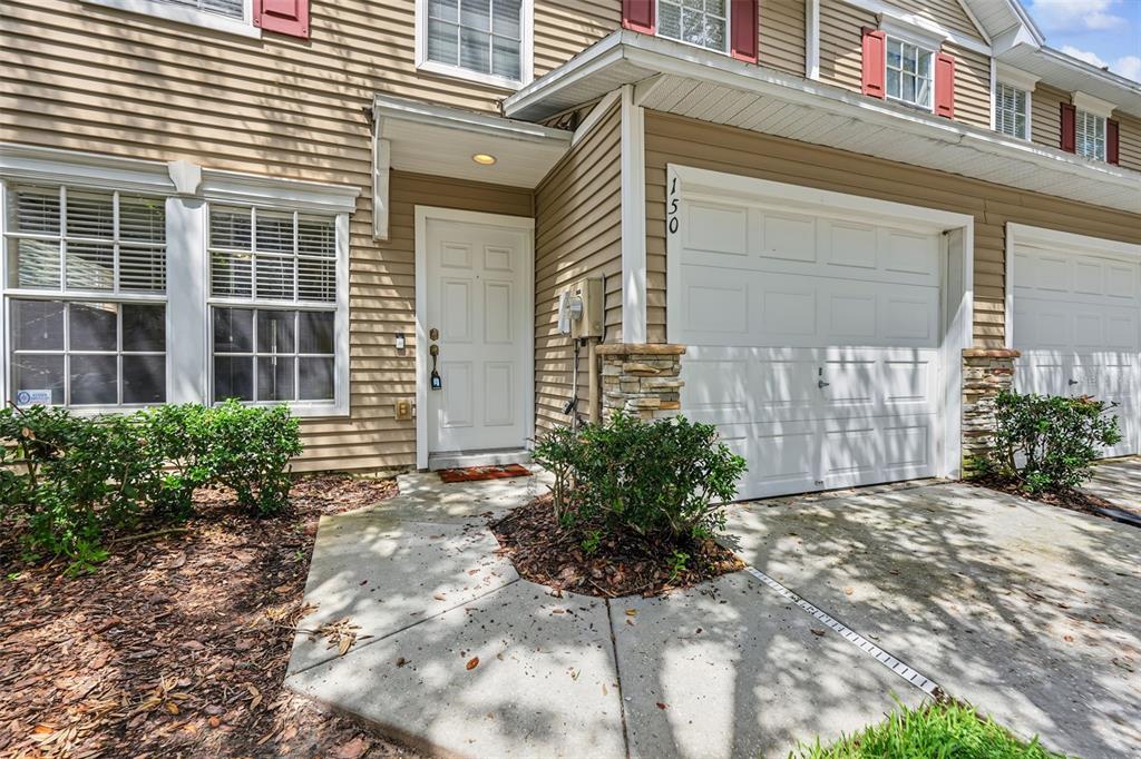 A tan-sided townhouse exterior features a white front door, a garage, and a concrete walkway — 150 SAWTOOTH DRIVE, VALRICO, FL