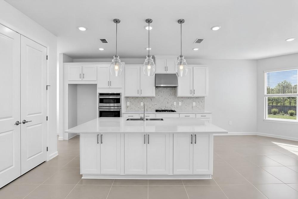 A modern kitchen features white cabinetry, a large quartz island, and stainless steel appliances — 14258 SAWMILL STREET, PARRISH, FL