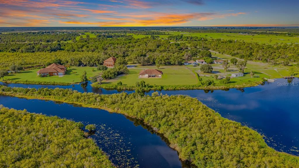 An aerial view shows houses situated on a grassy lot beside a winding river — 37511 WASHINGTON LOOP ROAD, PUNTA GORDA, FL