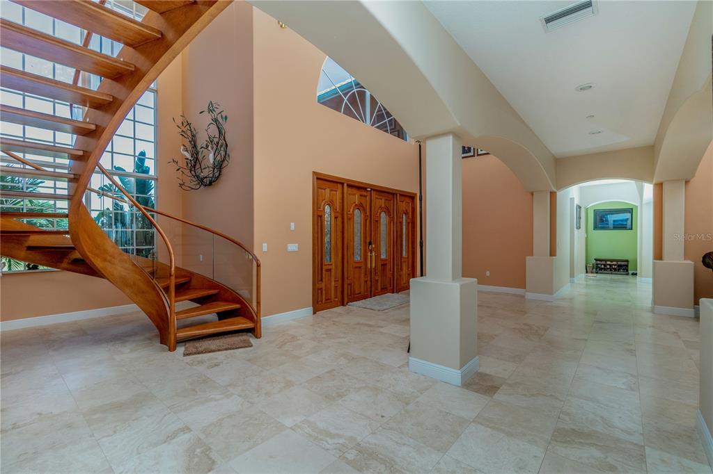 A spacious foyer features a curved wooden staircase, tile flooring, and arched architectural details — 37511 WASHINGTON LOOP ROAD, PUNTA GORDA, FL