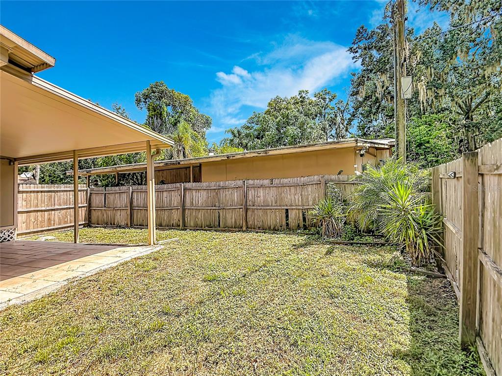 A backyard features a covered patio, a wooden privacy fence, and a grassy lawn — 14446 SHANGRILA LANE, ODESSA, FL