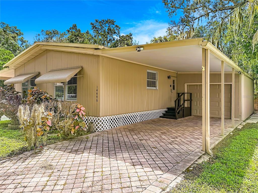 A tan mobile home features a paved carport, a lattice skirt, and metal window awnings — 14446 SHANGRILA LANE, ODESSA, FL