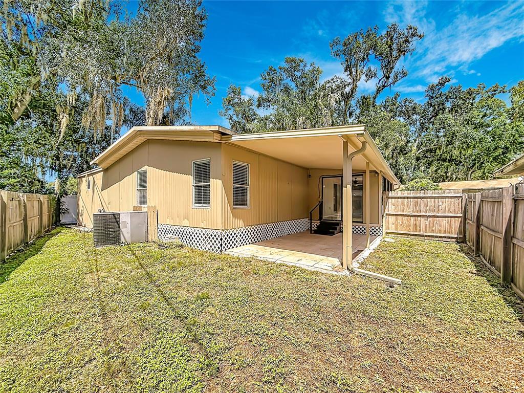 The exterior of a tan mobile home features a covered patio and a fenced backyard — 14446 SHANGRILA LANE, ODESSA, FL