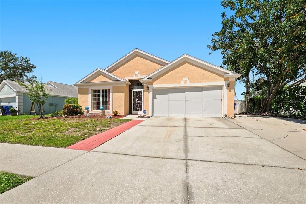 A single-story house with a tan stucco exterior, a two-car garage, and a concrete driveway — 207 LAKEWAY LANE, APOLLO BEACH, FL