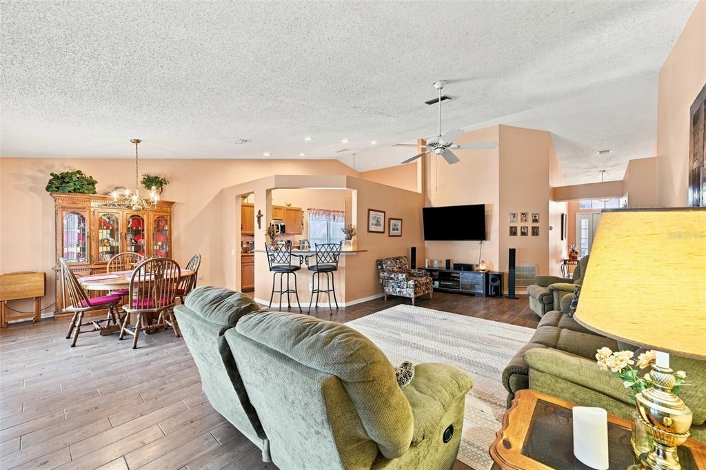 An open-concept living and dining area features wood-look flooring, peach walls, and a ceiling fan — 207 LAKEWAY LANE, APOLLO BEACH, FL