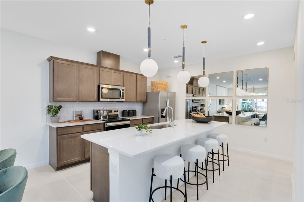 A modern kitchen features brown cabinetry, a white quartz island, and three pendant lights — 11547 HARBORVIEW STREET, ORLANDO, FL