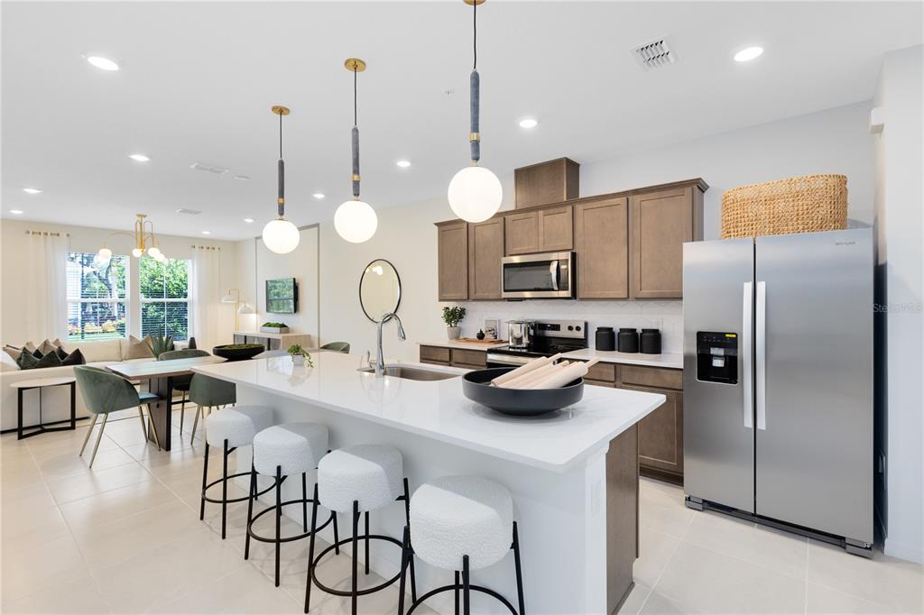 A modern kitchen features a white island with bar stools, stainless steel appliances, and wood cabinetry — 11547 HARBORVIEW STREET, ORLANDO, FL