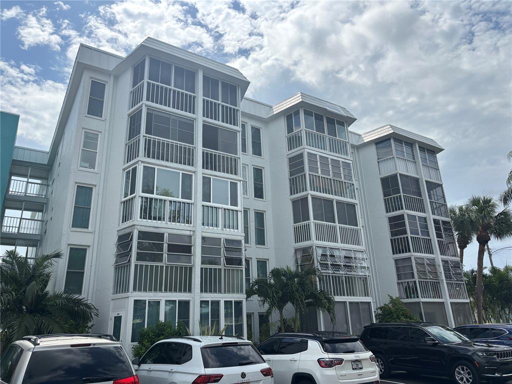 A multi-story white apartment building features screened-in balconies and a parking lot in front — 4910 38TH WAY S UNIT 411, ST PETERSBURG, FL