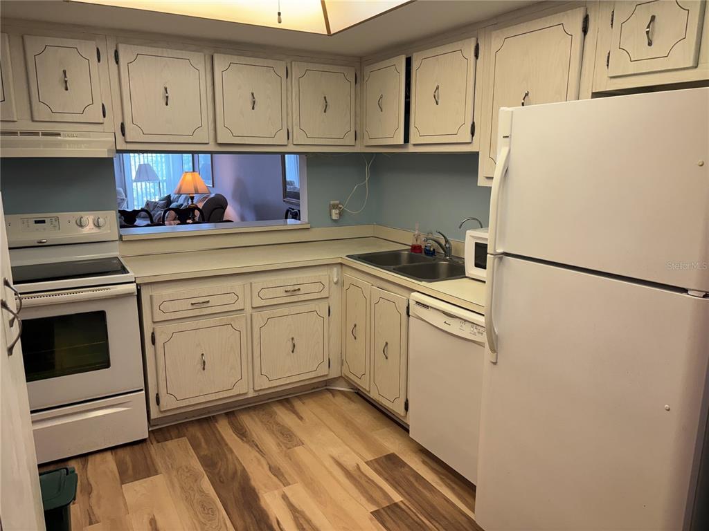 A kitchen features white cabinets, light-colored countertops, wood-look flooring, and white appliances — 4910 38TH WAY S UNIT 411, ST PETERSBURG, FL