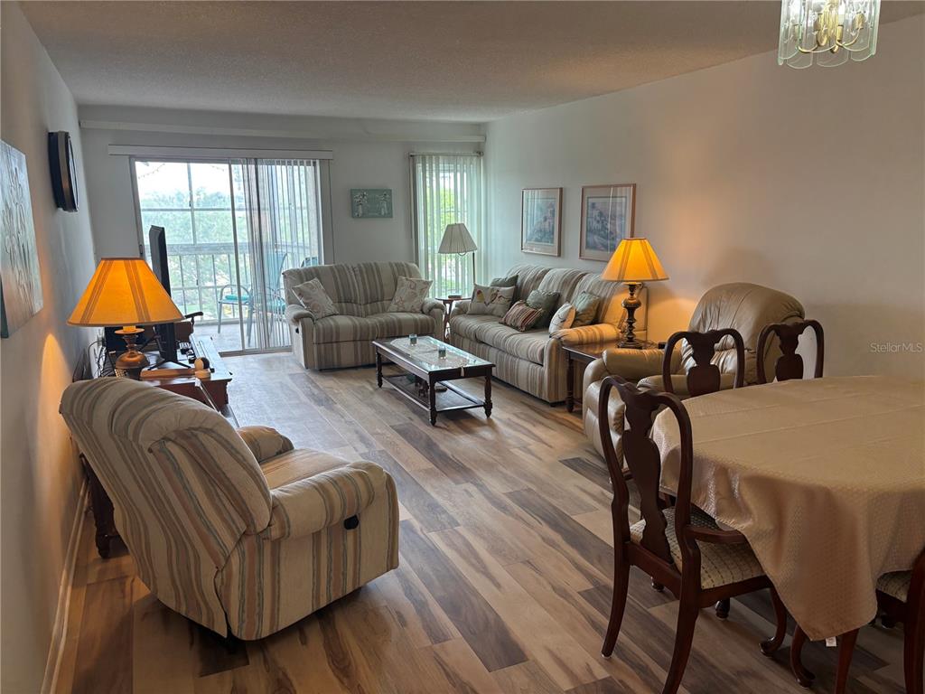 A living and dining area features wood-look flooring, neutral furniture, and a sliding glass door — 4910 38TH WAY S UNIT 411, ST PETERSBURG, FL