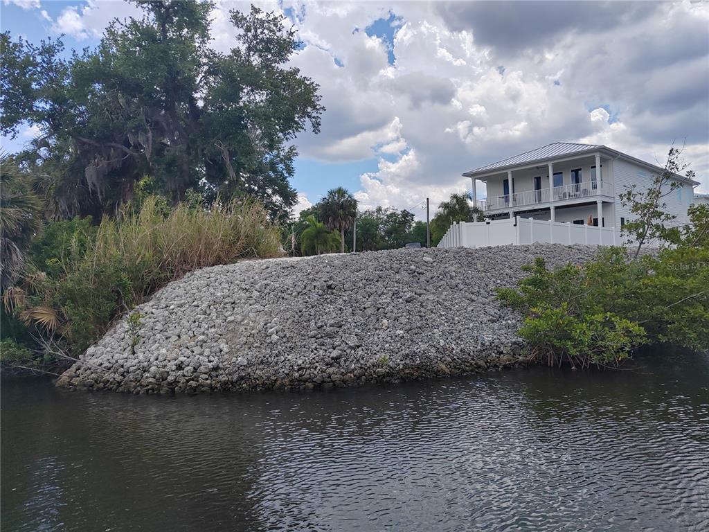 A house sits behind a large rock-covered embankment next to a body of water — 4623 3RD AVENUE E, BRADENTON, FL