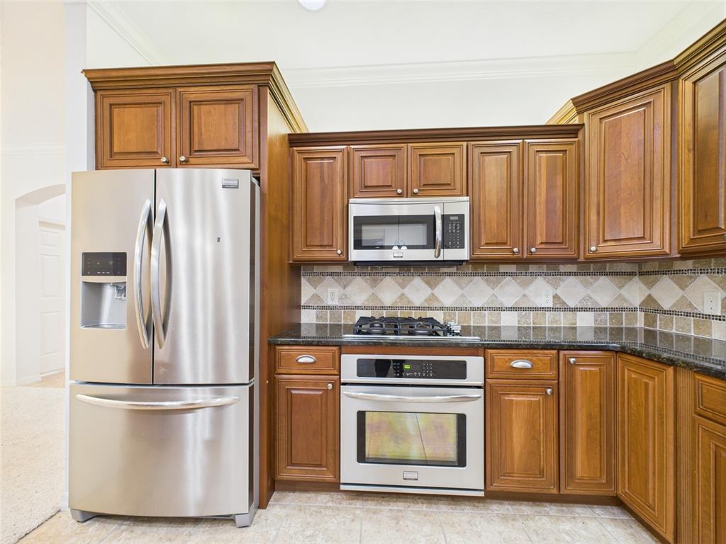 A kitchen features wood cabinets, stainless steel appliances, and a tiled backsplash — 375 SIMPSON STREET, THE VILLAGES, FL