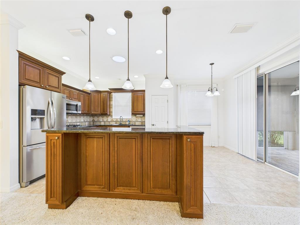 A kitchen features wood cabinets, a granite-topped island, stainless steel appliances, and tile flooring — 375 SIMPSON STREET, THE VILLAGES, FL