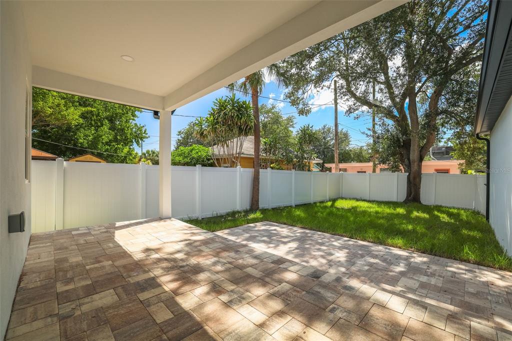 A covered patio with paver flooring overlooks a fenced backyard with a large tree — 1426 15TH STREET N, ST PETERSBURG, FL