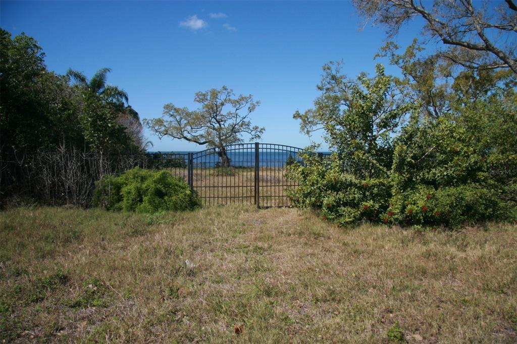 A metal gate stands in a grassy field, opening to a view of the ocean — 000 BLUFF BOULEVARD, HOLIDAY, FL