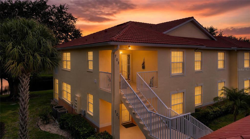 An exterior view of a two-story tan building with a red tile roof at sunset — 703 CASA DEL LAGO WAY UNIT 703, VENICE, FL