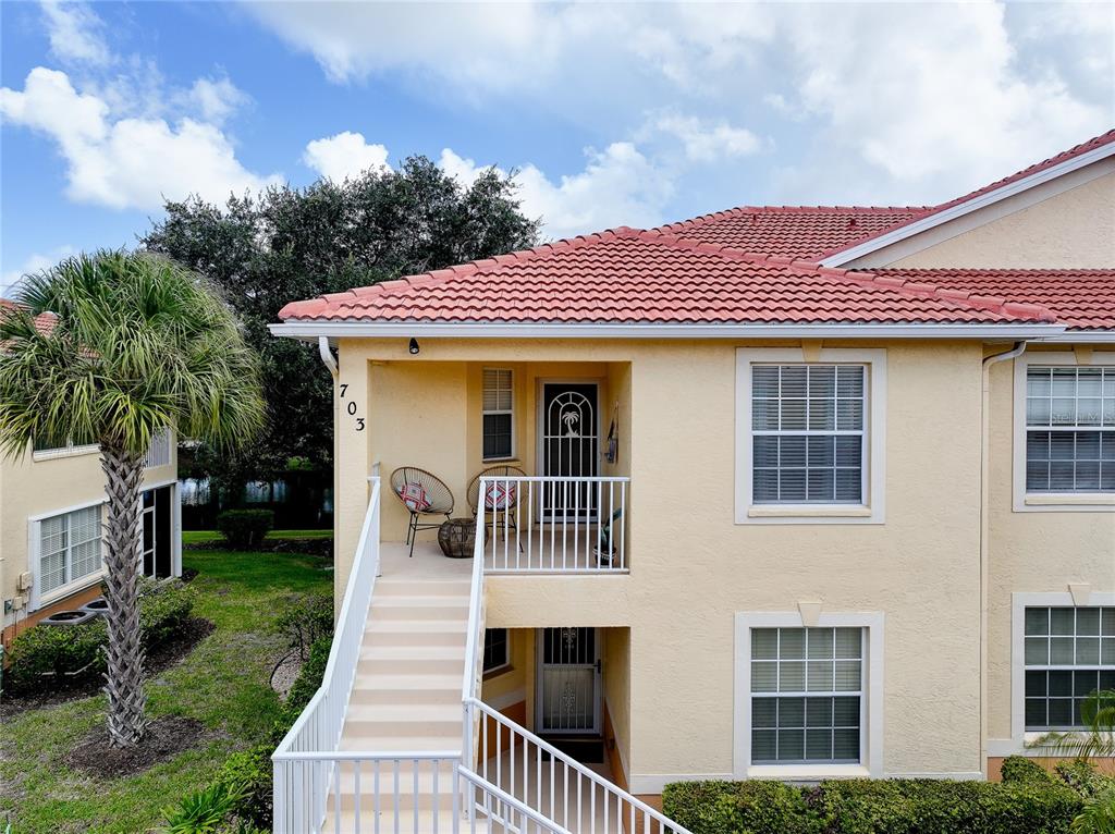 An exterior view of a two-story apartment building with a staircase leading to a balcony — 703 CASA DEL LAGO WAY UNIT 703, VENICE, FL