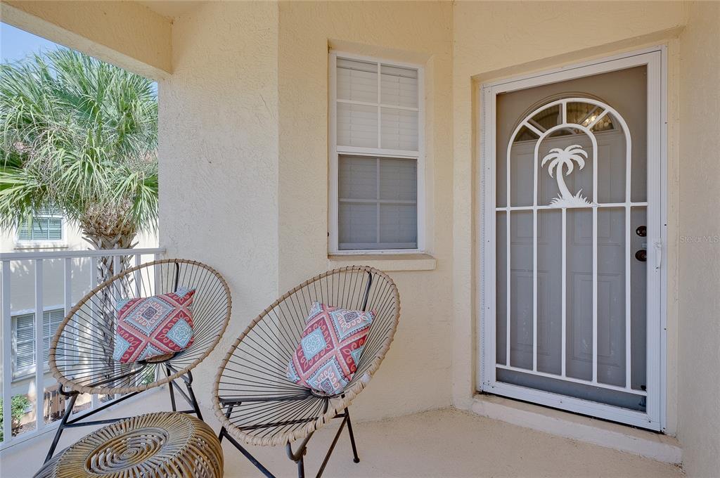 A balcony features two wire chairs with patterned pillows, a small table, and a screen door — 703 CASA DEL LAGO WAY UNIT 703, VENICE, FL