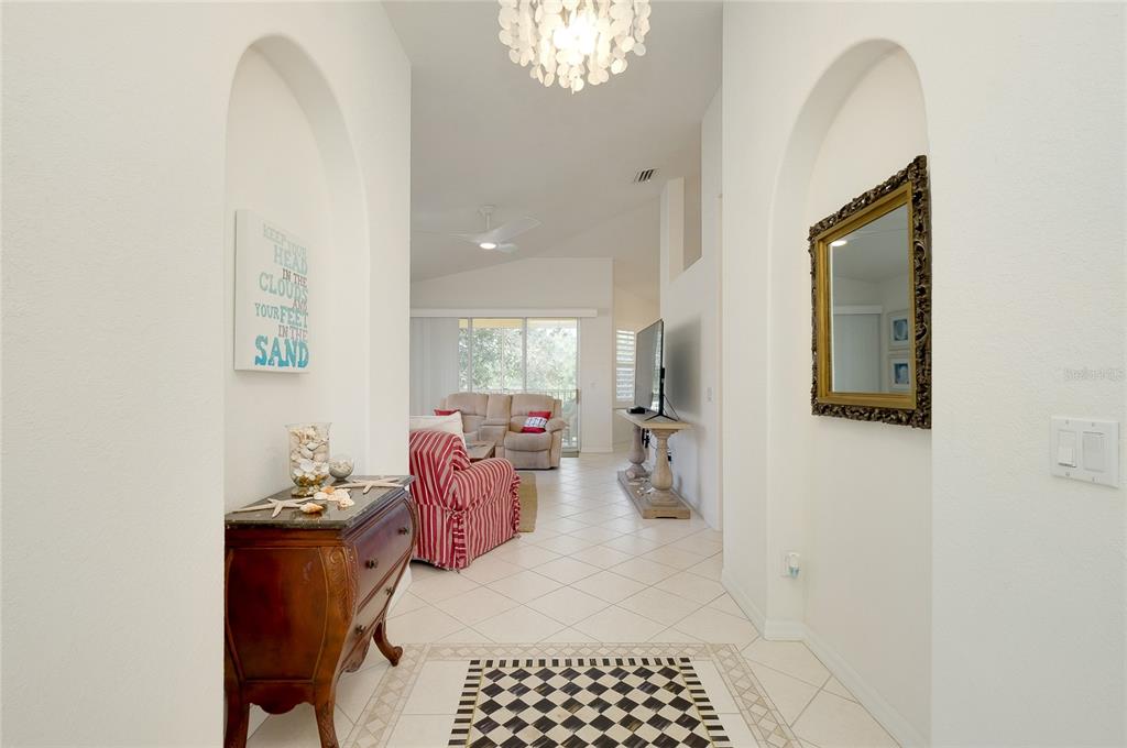 A tiled entryway leads into a living room with arched alcoves and a chandelier — 703 CASA DEL LAGO WAY UNIT 703, VENICE, FL