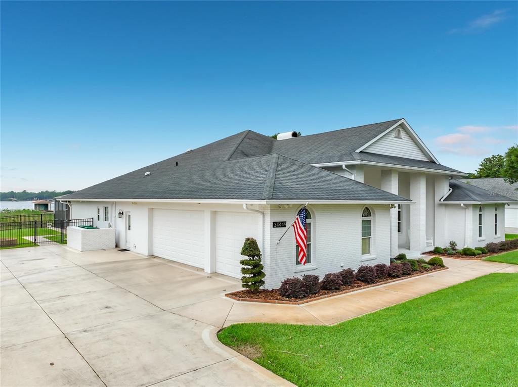 A white brick house with a multi-car garage and a large lawn near water — 34449 PARKVIEW AVENUE, EUSTIS, FL