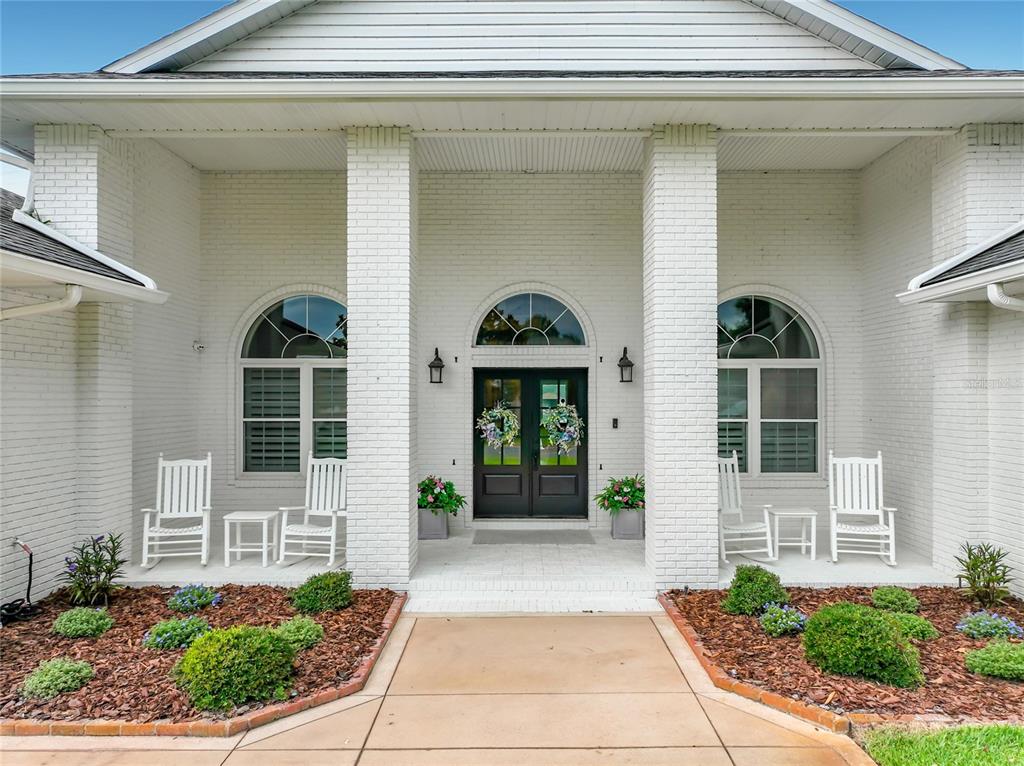 A white brick house exterior features a covered entryway with double doors and rocking chairs — 34449 PARKVIEW AVENUE, EUSTIS, FL
