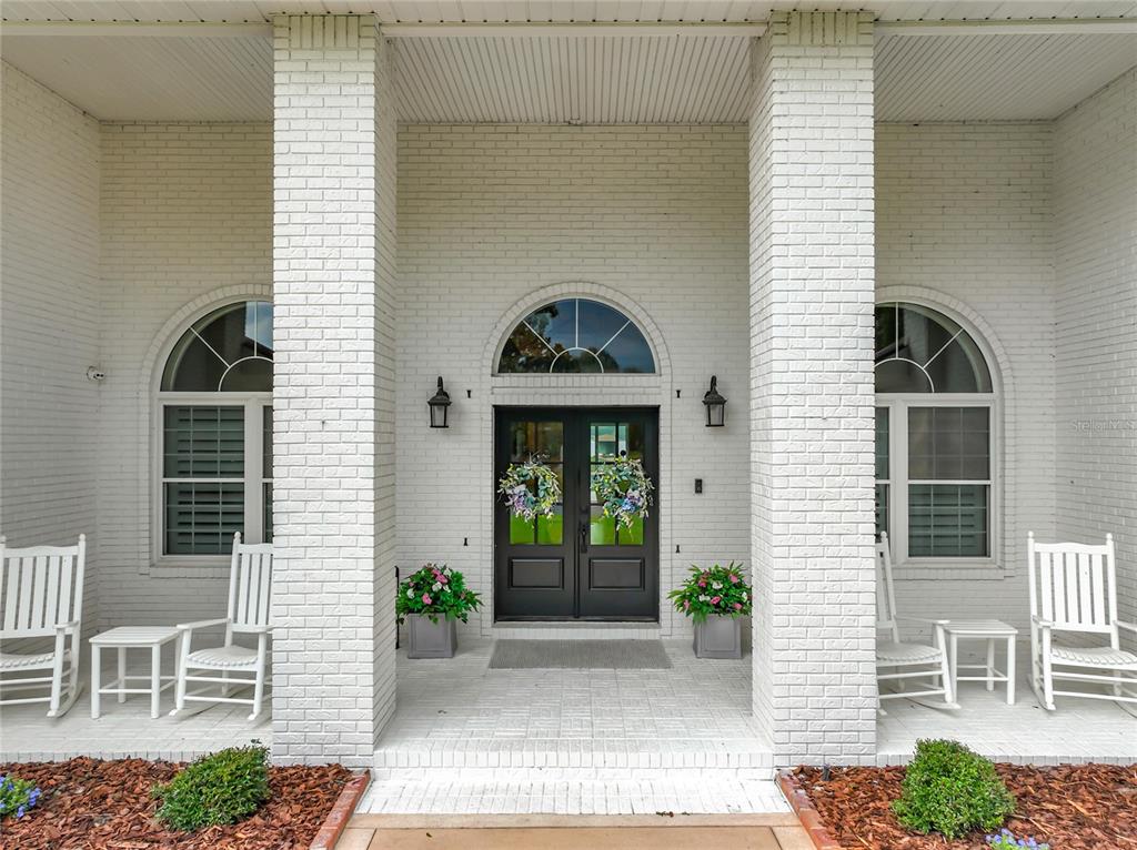 A white brick porch features a double front door, arched windows, and four rocking chairs — 34449 PARKVIEW AVENUE, EUSTIS, FL