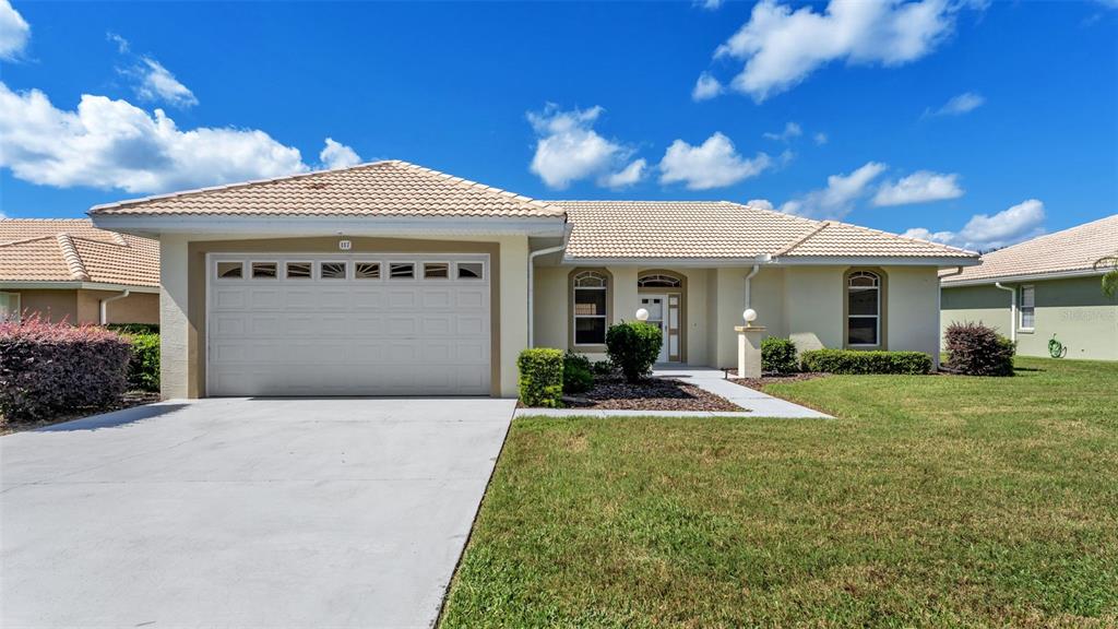 A single-story house with a white garage door, beige stucco walls, and a tiled roof — 117 HARBOR WAY, AUBURNDALE, FL