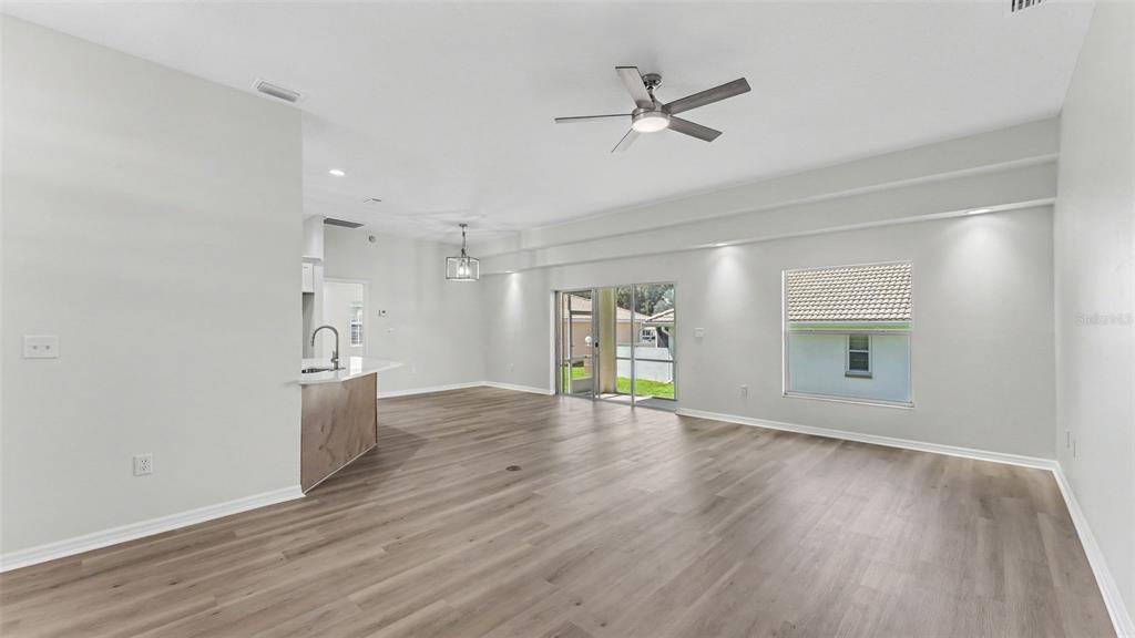 An empty living room features light wood-look flooring, a ceiling fan, and sliding glass doors — 117 HARBOR WAY, AUBURNDALE, FL