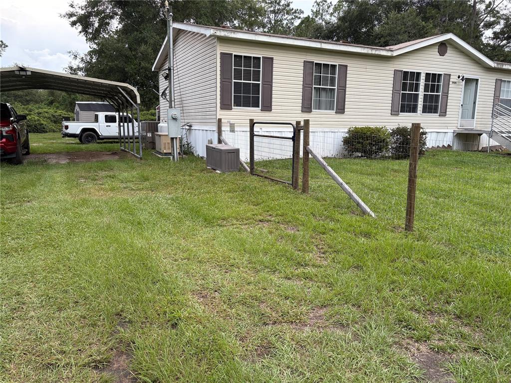 A single-story manufactured home with a metal carport, a white pickup truck, and wire fencing — 5828 BRYCE STREET, KEYSTONE HEIGHTS, FL