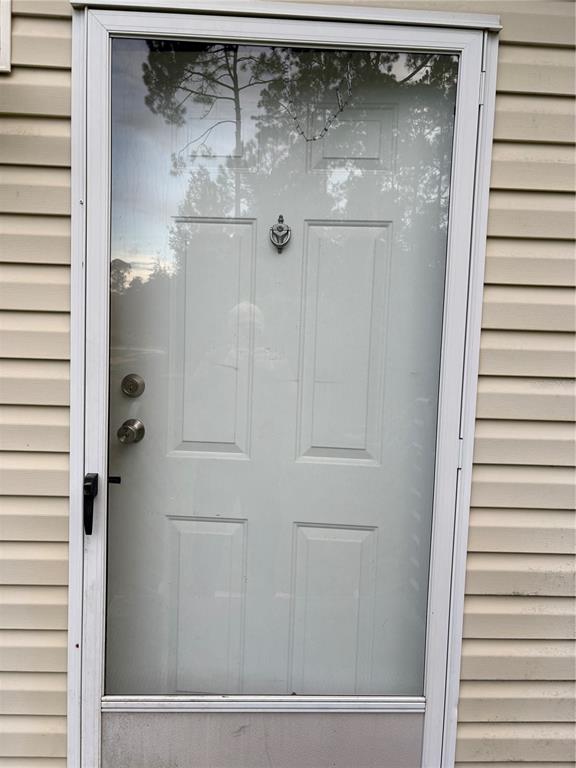 A white front door with a glass storm door is set against light-colored horizontal siding — 5828 BRYCE STREET, KEYSTONE HEIGHTS, FL