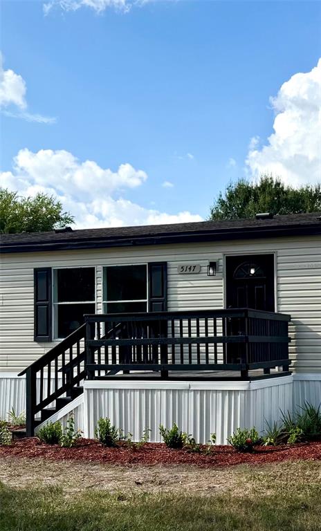 A tan manufactured home features a black wooden deck and stairs under a blue sky — 5147 ROCK DOVE LOOP, LAKELAND, FL