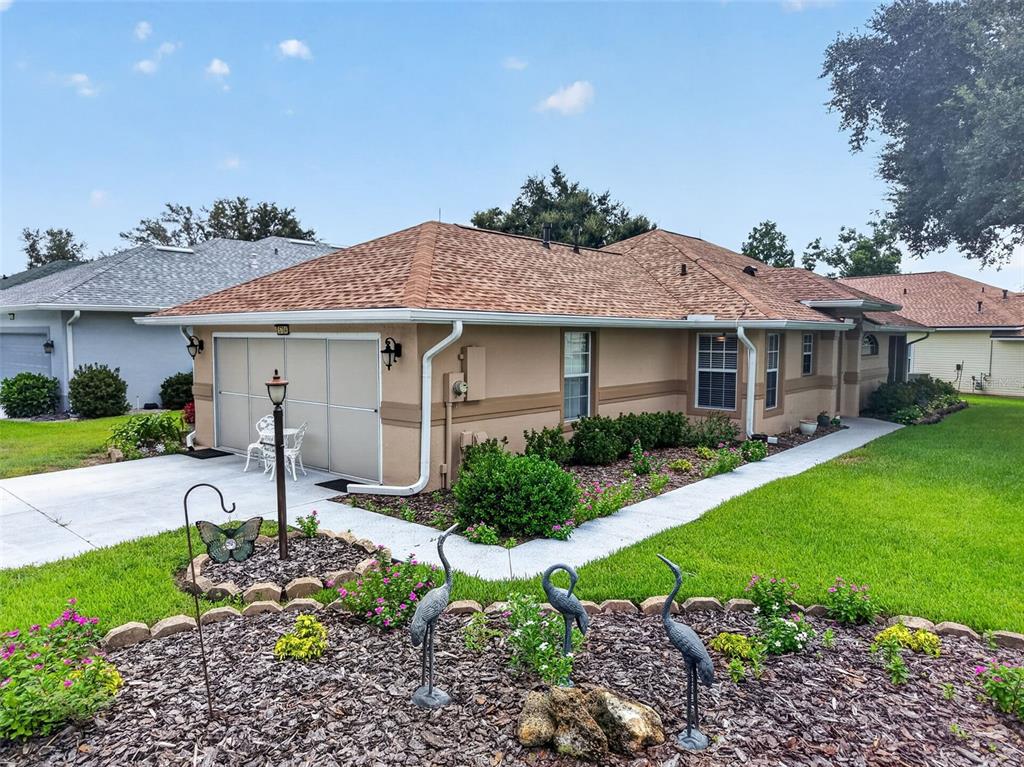 A tan single-story house features a brown shingled roof, a garage, and a landscaped yard — 5704 KING JAMES AVENUE, LEESBURG, FL