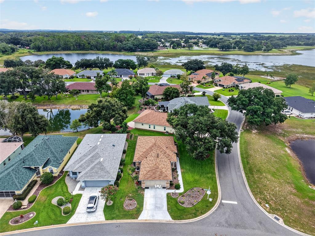 An aerial view shows suburban houses with shingled roofs situated near a lake — 5704 KING JAMES AVENUE, LEESBURG, FL