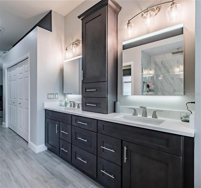 A bathroom features a double vanity with dark cabinets, white countertops, and two illuminated mirrors — 10131 PADDOCK OAKS DRIVE, RIVERVIEW, FL