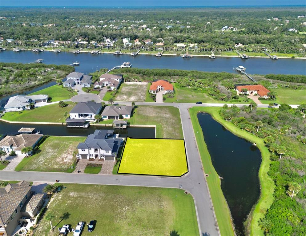 An aerial view shows a vacant, yellow-highlighted residential lot situated near a canal and pond — 61 MALIBU COVE, FLAGLER BEACH, FL