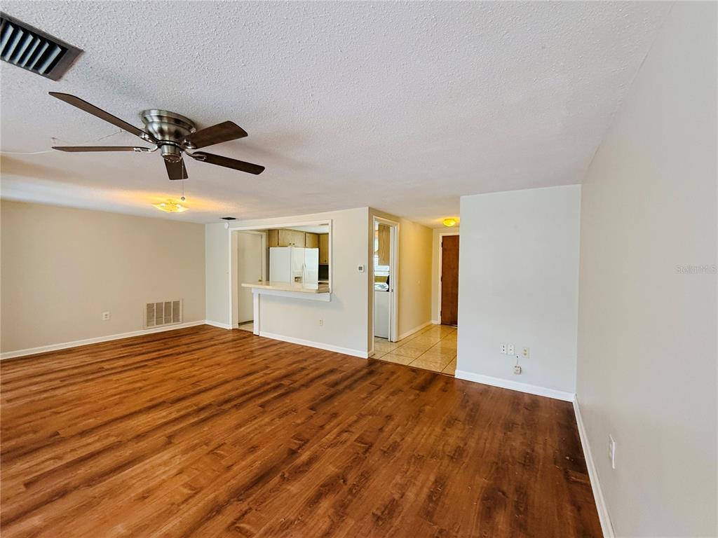 A living room with wood-look flooring, a ceiling fan, and an opening to the kitchen — 7910 LILAC DRIVE, PORT RICHEY, FL