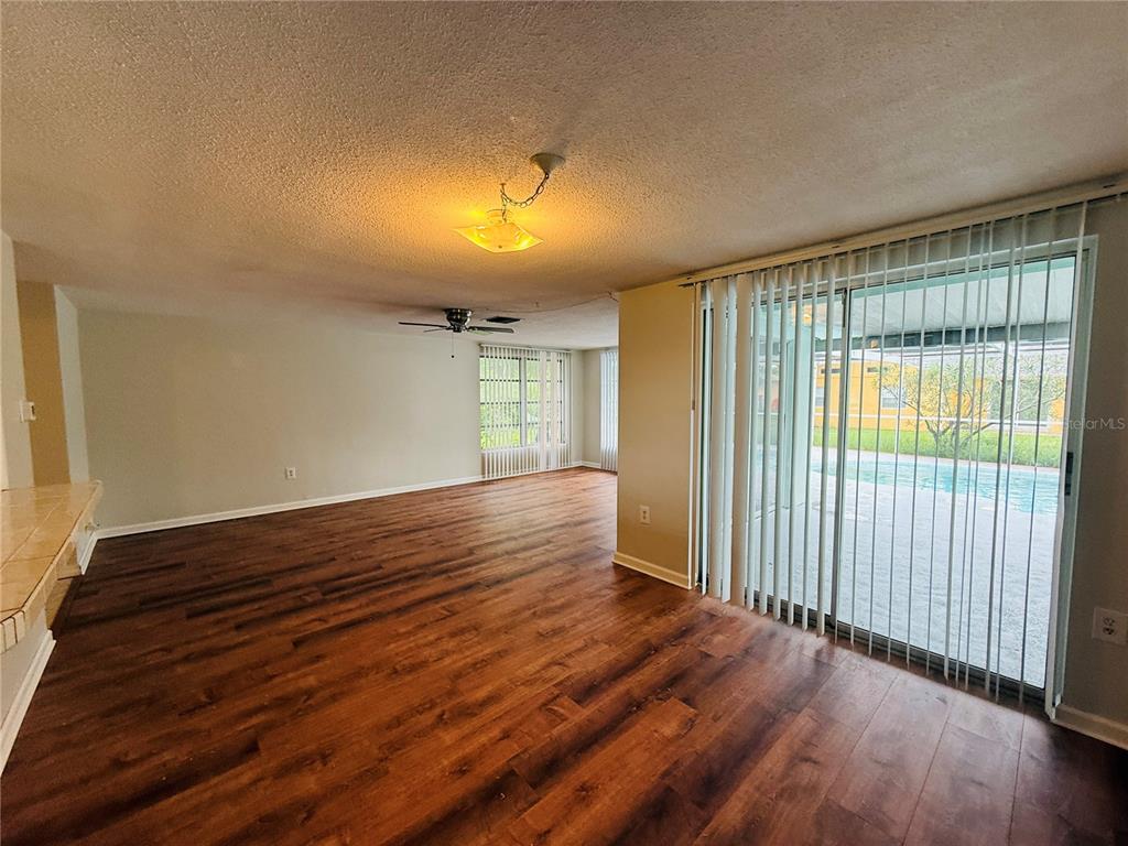 An empty living room with wood-look flooring, a ceiling fan, and sliding glass doors to a pool — 7910 LILAC DRIVE, PORT RICHEY, FL