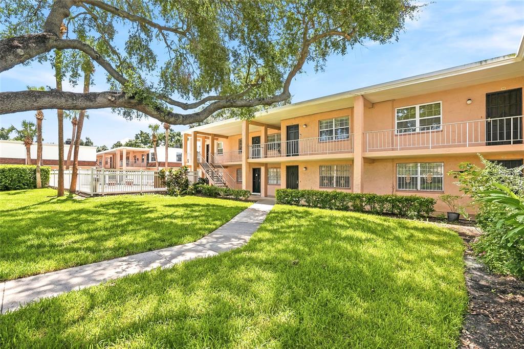 A two-story apartment building with a concrete walkway, green lawn, and large shade tree — 4702 MICHAEL COURT UNIT 142, TAMPA, FL