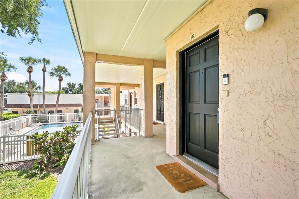 An exterior view of a second-floor apartment balcony with a black door and pool view — 4702 MICHAEL COURT UNIT 142, TAMPA, FL