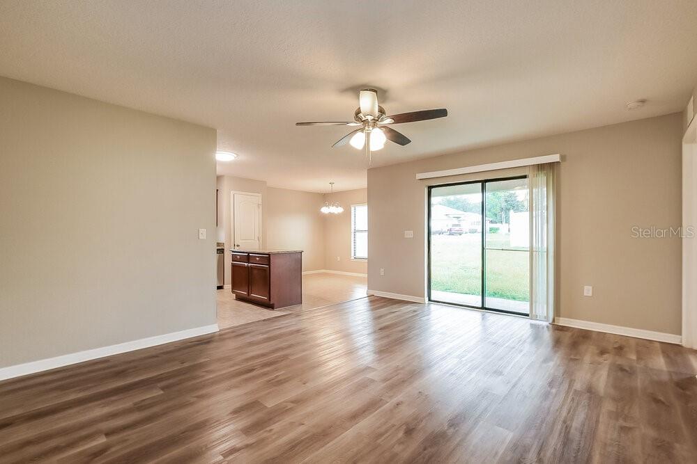 An open-concept living area with wood-look flooring, a ceiling fan, and sliding glass patio doors — 4292 ABACO DRIVE, TAVARES, FL