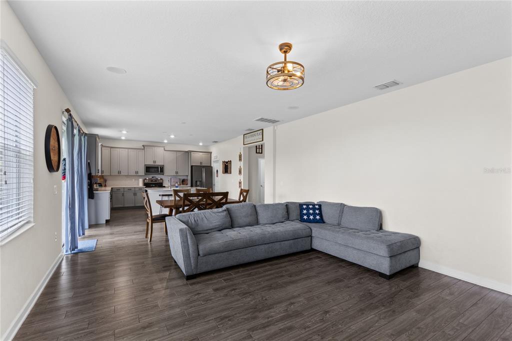 An open-concept living and dining area features dark wood flooring, a grey sofa, and a television — 12016 FICTION AVENUE, ORLANDO, FL